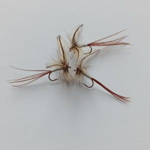Pode incluir: Quatro iscas de pesca com mosca brancas e marrons com penas vermelhas e brancas.