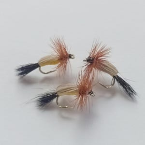 May include: Three brown and tan fly fishing lures with black and white feathers and a silver hook.