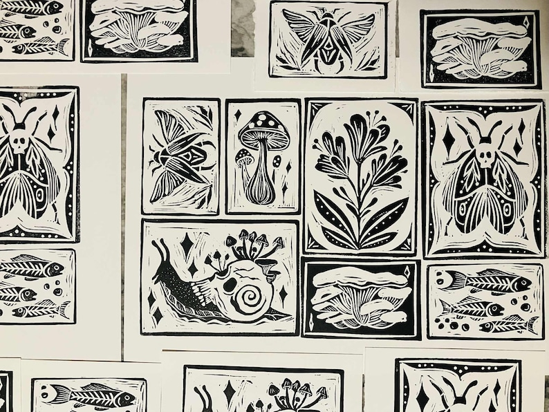 Peut inclure: Ensemble de linogravures en noir et blanc repr&eacute;sentant des motifs inspir&eacute;s de la nature. Les impressions incluent des insectes, des champignons, des fleurs, des squelettes de poissons et un escargot avec un cr&acirc;ne. L'&oelig;uvre est pr&eacute;sent&eacute;e sur fond blanc.