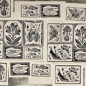 Peut inclure: Ensemble de linogravures en noir et blanc repr&eacute;sentant des motifs inspir&eacute;s de la nature. Les impressions pr&eacute;sentent des champignons, des squelettes de poissons, des insectes, des plantes et des escargots. Chaque tirage est rectangulaire avec un bord noir.