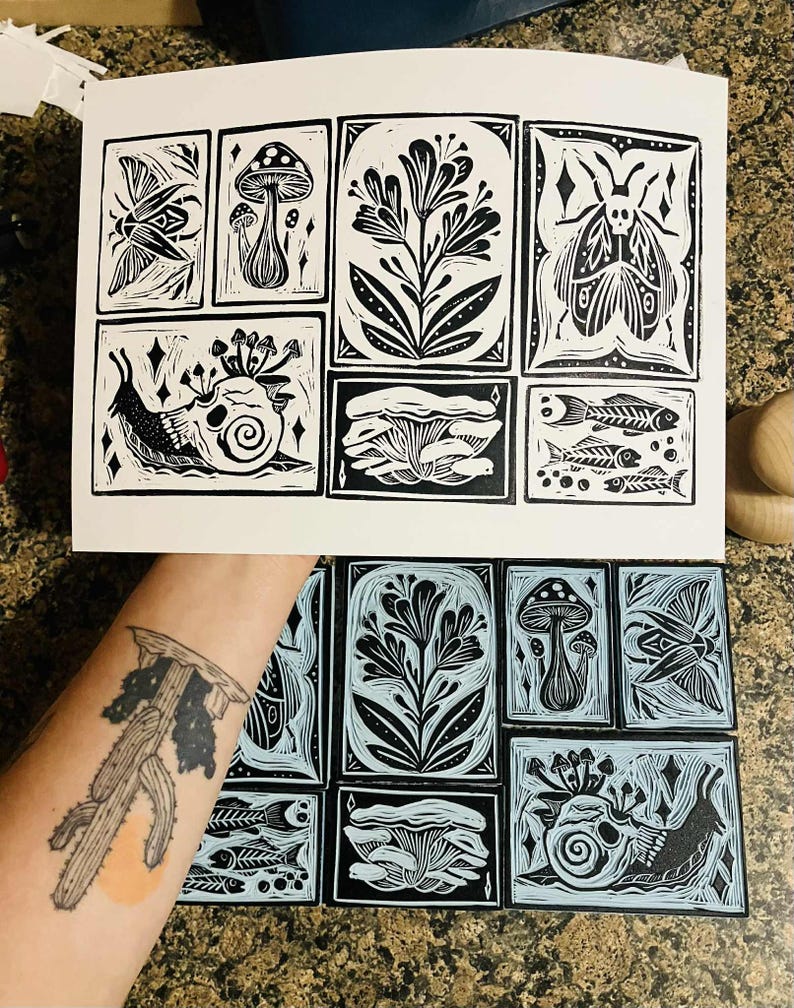 Peut inclure: Estampes en linogravure en noir et blanc repr&eacute;sentant des motifs botaniques et d'insectes. Les estampes comprennent des images de champignons, de fleurs, d'un papillon de nuit, d'un escargot avec un cr&acirc;ne et de squelettes de poissons. Les estampes sont affich&eacute;es sur fond blanc.