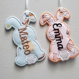 Op de afbeelding: Twee gepersonaliseerde bunny-vormige stoffen ornamenten, een lichtblauwe met de naam "Matteo" en de andere roze met de naam "Emma".
