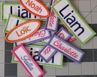 Puede incluir: Una colección de etiquetas de nombre de tela bordada de colores con varios nombres, incluyendo Liam, Noah, Loic, Charlotte y Faisa.