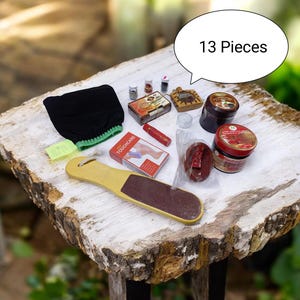 Peut inclure: Un ensemble de soins de 13 pièces comprenant un gant exfoliant noir à bordure verte, une râpe à pied en bois, une boîte rouge Touchcare, deux pots avec étiquettes rouges, un savon rouge sous plastique, un rouge à lèvres et divers flacons.
