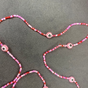 Może przedstawiać: Trzy różowe i czerwone koraliki naszyjniki z różowymi i czarnymi oczami.