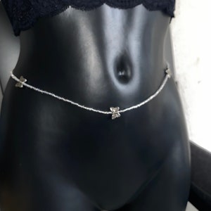 May include: A silver body chain with butterfly charms. The chain is made of small beads and is designed to be worn around the waist.