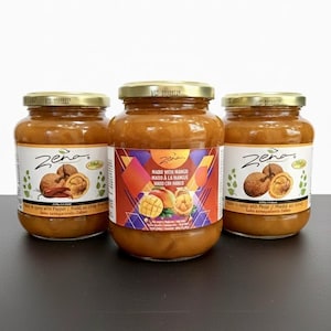 Puede incluir: Tres frascos de vidrio de jarabe de mango Zena con tapas doradas. Los frascos tienen etiquetas con texto en varios idiomas, incluyendo "Mabd with Mango" y "Madd au sirop". Los frascos están llenos de un líquido espeso de color marrón anaranjado.