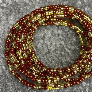May include: A waist bead necklace made of brown and gold beads. The beads are strung together in a continuous loop and are arranged in a pattern of alternating colours.