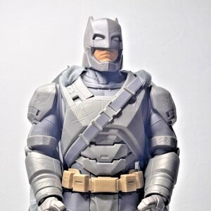 May include: Armoured Batman action figure in a display box. The figure is mainly grey with a tan belt and a dark blue cape. The box features the text "Batman v Superman" and "Big Figs".
