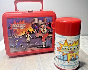 May include: A vintage red plastic lunchbox and matching flask featuring a space-themed graphic with the text "Lazer Tag". The lunchbox has a handle and a metal clasp. The flask has a red lid and a white and blue graphic.