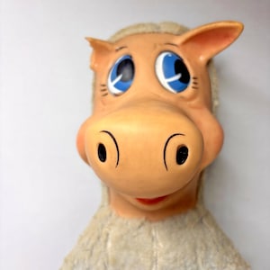 Op de afbeelding: Een vintage paardenhoofdmasker met een bruin gezicht, grote blauwe ogen en een rode mond. Het masker heeft een zachte, pluche manen en oren. Het algehele ontwerp is cartoonachtig en grillig, waarschijnlijk voor een kinderkostuum of spel.