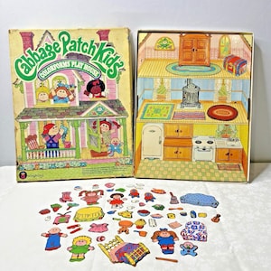 Puede incluir: Juego vintage de Cabbage Patch Kids Colorforms Play House. La caja presenta una ilustración de una casa con personajes de Cabbage Patch Kids. Incluye un interior de casa de juegos y varias pegatinas de personajes y muebles.