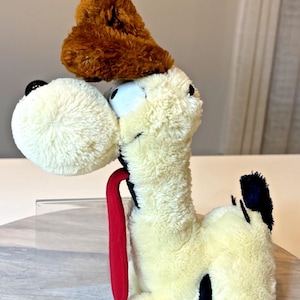 May include: A plush dog toy with a cream-colored body, a brown head, and black spots. It has a large, fluffy white head, a red tongue, and black eyes. The toy is soft and cuddly, perfect for children.