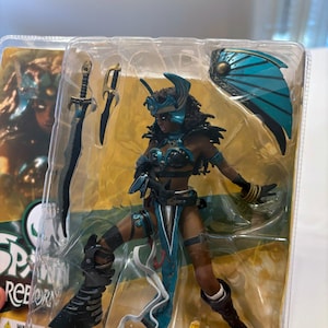 May include: Action figure of a female warrior in a teal and black outfit, with a matching helmet and shield. The figure is holding a sword and dagger. The packaging includes the words "Spawn Reborn".