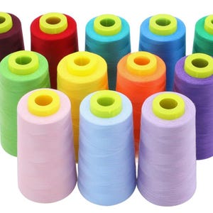 May include: A collection of colorful thread spools. The spools are in various colors, including red, green, blue, yellow, orange, and purple. Each spool has a yellow top and a light green center. The threads are tightly wound.