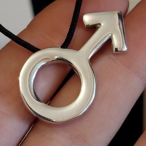 May include: A silver pendant necklace with a male symbol charm. The pendant is on a black cord.