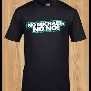 以下が含まれることがあります： 「NO MICHAEL, NO NO!」の文字が白と水色の縁取りでプリントされた黒いTシャツ。木製の背景に配置されています。