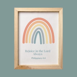 May include: A framed print with a rainbow design in shades of peach, yellow, blue, and gray. The print includes the text "Rejoice in the Lord Always Philippians 4:4".