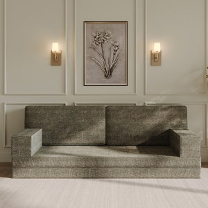 Op de afbeelding: Een moderne woonkamer met een grijze bank, een ingelijste botanische print en een bijzettafel met een marmeren blad. De kamer is ingericht met een vaas met droogbloemen en een vloerkleed, wat een neutrale en uitnodigende sfeer creëert.