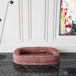 May include: A plush, oval-shaped dog bed with a brown, textured fabric. The bed is sitting on a black and white marble floor.