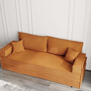 May include: A brown fabric sofa with three cushions. The sofa has a tufted design and is sitting on a wooden floor.