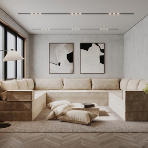 May include: A large, light brown sectional sofa with multiple cushions sits in a modern living room with a light gray wall, a wood floor, and two abstract black and white paintings.