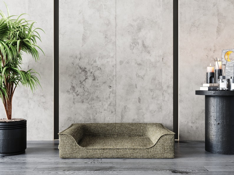 Peut inclure: Un panier pour chien beige avec une texture tiss&eacute;e, plac&eacute; devant un mur gris. Le lit a un profil bas avec des c&ocirc;t&eacute;s sur&eacute;lev&eacute;s. Un pot de plante et une petite table avec des bougies et des ornements sont &eacute;galement visibles.