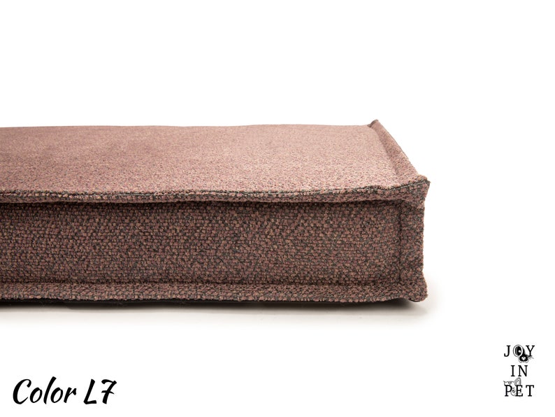 May include: A close-up of a dog bed in a muted mauve color. The bed has a rectangular shape with a thick, textured fabric. The edges are neatly sewn, and the overall design is simple and functional. The words 'Color L7' are printed in black at the bottom left.