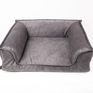 Puede incluir: Una cama para perro rectangular gris con un borde elevado y una tela suave y mullida. La cama tiene un interior profundo y acolchado para mayor comodidad.