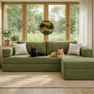 Puede incluir: Un sofá seccional verde con dos cojines blancos. Un gato negro y un gato naranja descansan en el sofá. La habitación tiene grandes ventanas, cortinas y una alfombra tejida.