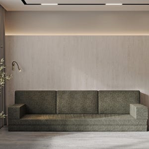 Könnte beinhalten: Ein grünes Ecksofa mit einer hellbraunen Wand dahinter. Das Sofa hat ein schlichtes Design und ist aus einem weichen, bequemen Stoff gefertigt.