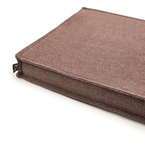 Op de afbeelding: Een rechthoekig dierenbed in een gedempte bruine kleur. Het bed heeft een textuurstof en een gestikte rand. Een klein zwart label met witte tekst is aan de hoek bevestigd. Het bed is ontworpen voor huisdieren.