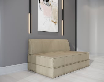 May include: A beige fabric sofa bed with a light wood floor and a black and white abstract painting on the wall behind it.