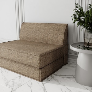 Op de afbeelding: Een bruine stoffen futonbank met een eenvoudig ontwerp. De bank staat op een witte marmeren vloer.