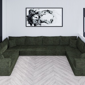 May include: A large, dark green sectional sofa with multiple cushions. The sofa is arranged in a U-shape and sits on a light wood floor. A black and white abstract painting hangs on the wall behind the sofa.