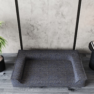 May include: A blue and gray dog bed with a raised rim and a textured fabric. The bed is sitting on a wooden floor.