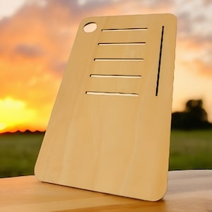 Puede incluir: Una tabla de cortar de madera marrón claro con cinco ranuras horizontales y un agujero redondo en la esquina superior. La tabla está sobre una superficie de madera.