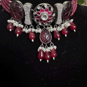 May include: A silver and burgundy choker necklace with a floral design and dangling teardrop-shaped stones.