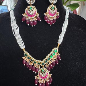 May include: A white pearl necklace with a green and pink pendant and matching earrings. The pendant features a large, ornate design with green and pink stones. The earrings are also ornate and feature green and pink stones.