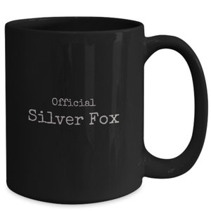 May include: Black ceramic coffee mug with a white inscription that reads "Official Silver Fox".