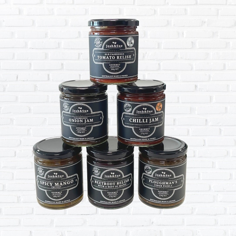 May include: Six glass jars of gourmet condiments with black labels and white text. The jars are arranged in a pyramid shape. The labels read: Old Fashioned Tomato Relish, Onion Jam, Chilli Jam, Spicy Mango Chutney, Beetroot Relish with a Hint of Maple, and Ploughman's Cider Pickle.