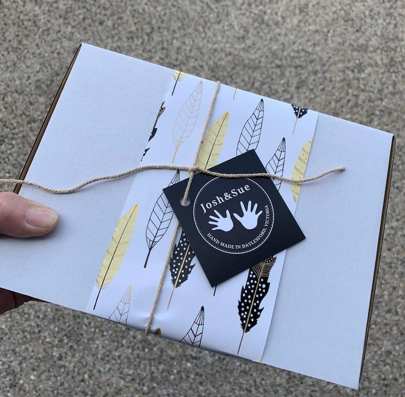 May include: A white gift box with a black and gold feather pattern. The box is tied with twine and has a black tag that says "Josh & Sue" with a handprint logo and the text "Hand Made in Daylesford, Victoria".