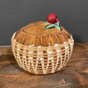 May include: A ceramic jar with a woodgrain pattern and a white woven design. The lid has a red cherry on top.