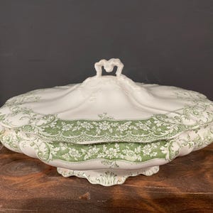 May include: A white porcelain serving dish with a green floral pattern and a lid with a decorative handle.