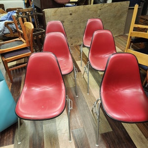 May include: Five red chairs with black trim and silver legs. The chairs are arranged in a row on a wooden floor.