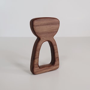 Könnte beinhalten: Ein Holz-Beißring in Form einer Sanduhr für Babys. Der Beißring ist aus Naturholz gefertigt und hat eine glatte, abgerundete Oberfläche.