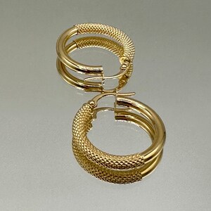 May include: A pair of gold hoop earrings with a textured design. The earrings are made of a thick, round wire and have a hinged closure.