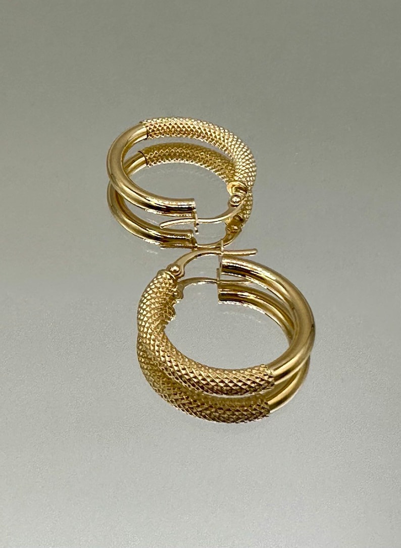 May include: A pair of gold hoop earrings with a textured design. The earrings are made of a thick, round wire and have a hinged closure.