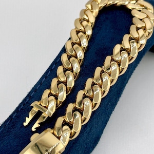 May include: A gold curb chain bracelet with a clasp closure. The bracelet is on a blue velvet surface.