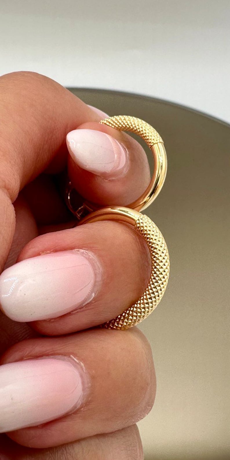 May include: Two gold hoop earrings with a textured surface. The earrings are stacked on top of each other.